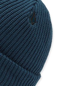 Bonnet tricoté en bleu canard avec une texture côtelée et un revers replié. Il présente un petit logo noir brodé sur le côté.