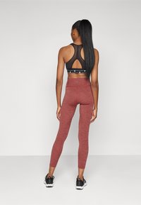 Soutien-gorge de sport noir avec un dos en forme de trou de serrure, associé à un legging bordeaux ajusté avec une texture chinée et des coutures contrastantes.