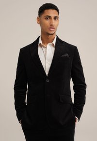 Zwarte corduroy blazer met reverskraag, twee voorzakken, enkele knoopsluiting en een zakdoek in de borstzak.