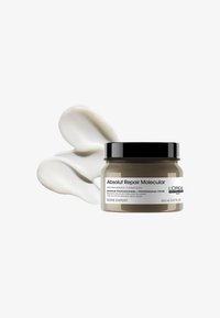 Donkergrijze container met een zwart deksel, gelabeld "Absolut Repair Molecular." Crèmewitte haarmasker weergegeven naast de pot.
