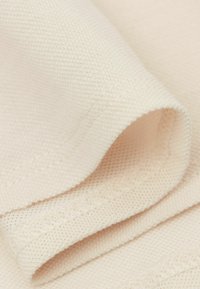 Hellbeiger Stoff mit einer strukturierten Webart, gefaltet, um die Dicke und die Nahtdetails entlang der Kanten zu zeigen. Weiches und glattes Erscheinungsbild.