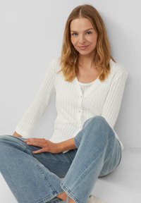 Witte geribbelde cardigan met een V-hals en knopen, gecombineerd met lichtblauwe wijde jeans. Glad materiaal, casual ontwerp en driekwart mouwen.
