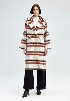 Kreemjas, pruunis ja punases värvitoonis ruuduline villane mantel, millel on lõhikuga krae, kahekordne nööbistamine ja küljetaskud. Kantud tumedate pükste peal.