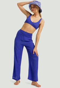 Royal blue ribbed crop top dengan celana lebar yang serasi; kain ringan dengan pinggang elastis. Dipasangkan dengan topi ember bergaris.