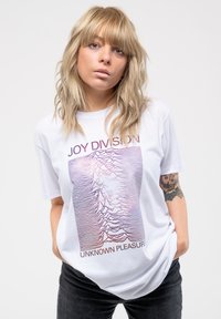 White short-sleeve t-shirt featuring purple and black graphic design with "JOY DIVISION" and "UNKNOWN PLEASURES" text. Soft cotton material.