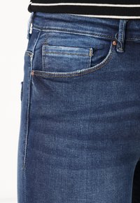 Denim kavbojke v temno modri pranju z običajnim pasom, sprednjimi in zadnjimi žepi ter subtilnim zbledelostjo na stegnih.