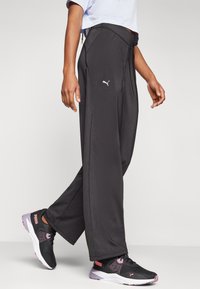 Zwarte sportbroek van Puma met een losse pasvorm, gemaakt van gladde stof, voorzien van een wit logo en gedetailleerde stiksels. Gecombineerd met zwart-roze hardloopschoenen.