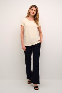 Cream short-sleeve t-shirt with a scoop neck, paired with dark flared jeans. The model wears black slide sandals, showcasing a casual outfit.
