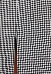 Tissu à motif pied-de-poule noir et blanc avec une fente verticale révélant un matériau marron en dessous.