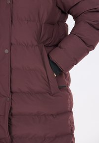 Bordeaux farvet polstret frakke med et quiltet design, der har en sidelomme og sorte manchetter. Fremstillet af blødt, isoleret materiale.