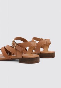 Sandalias de cuero marrón con tiras cruzadas, hebilla ajustable y un bajo tacón de madera, que ofrecen un acabado texturizado.