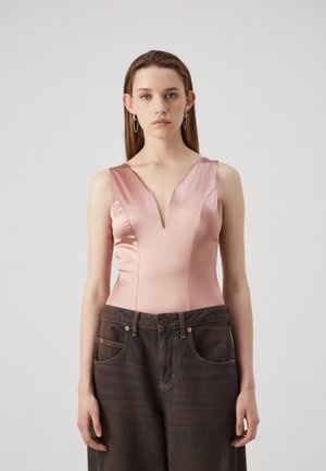 Pink satin bodysuit with a deep V-neck and wide shoulder straps, paired with dark, loose-fitting denim jeans featuring visible stitching.