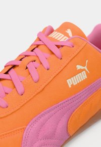 Orangene Wildleder-Sneaker mit pinken Schnürsenkeln und Akzenten. Verfügt über ein strukturiertes Design und ein weißes Puma-Logo an der Seite. Feste Gummisohle.