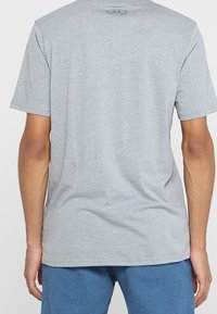 Grå kortärmad T-shirt i bomull, med rund hals och en logodetalj på övre ryggen, som visar en avslappnad passform.