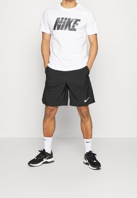 Vit t-shirt med svart "NIKE"-logotyp, svarta träningsshorts, vita strumpor och svarta sneakers. Avslappnad sportklädsel med en bekväm passform.