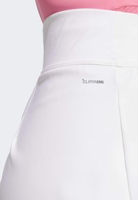 Vita atletiska byxor i vitt med en slät yta och bred midjeband, med en "ClimaCool"-logotyp tryckt i grått på sidan.
