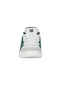 Bílé sportovní tenisky s zelenými semišovými akcenty, texturovaným páskem a bílými tkaničkami; mají logo na jazyku a polstrovanou podrážku.