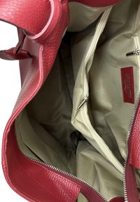 Czerwona skórzana torebka o fakturowanej powierzchni, rozzipowana, ukazująca beżowe wnętrze z materiału, wyposażona w kieszenie na zamek i otwarte przegródki.