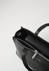 Borsa nera in pelle con forma rettangolare, chiusura con zip e doppi manici. Presenta una cerniera argento e un logo del marchio discreto. Texture liscia.