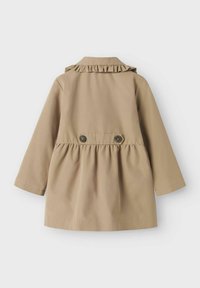 Bež kaput s volanom na ovratniku, dugim rukavima i skupljenim strukom. Ima dva smeđa dugmeta na stražnjoj strani. Glatka tkanina.