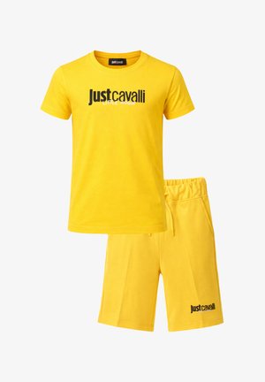 Set composto da T-shirt gialla a maniche corte e pantaloncini abbinati con la scritta "Just Cavalli Little Rogue" stampata in bianco e nero sul davanti di entrambi i capi.
