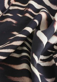 Tissu à motif zèbre présentant de larges rayures noires et écrues avec des textures subtiles. Matériau doux en mélange avec une apparence drapée.