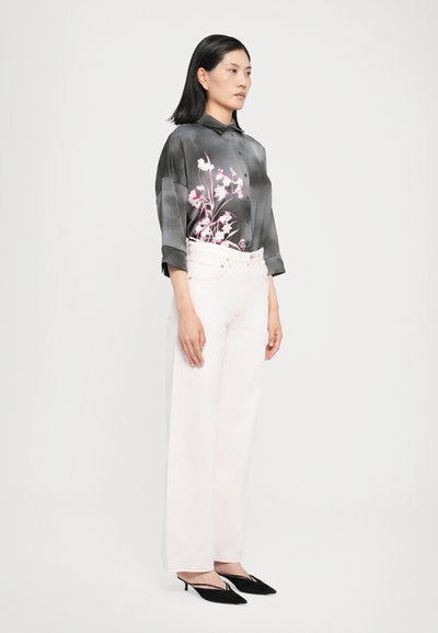 Bluză florală alb-negru cu guler, combinată cu blugi albi cu talie înaltă și pantaloni largi, împreună cu tocuri slingback negre.