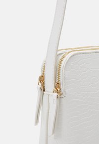 Borsa in pelle sintetica bianca con finitura testurizzata, doppia cerniera dorata e tracolla. Le cerniere sono dotate di piccoli tiranti in pelle.