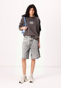 Gray, oversized sweatshirt with logo, paired with black and white denim shorts. Model wears beige sneakers and holds a blue strap bag.