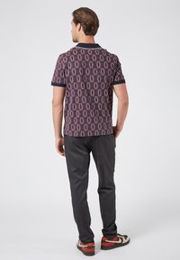 Camisa de manga corta con estampado en tonos oscuros, que presenta un diseño geométrico. Combinada con pantalones oscuros ajustados y zapatillas multicolores.