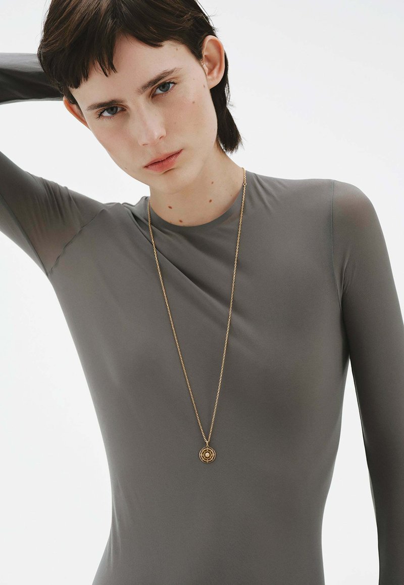 Bodysuit gris de manga larga y ajuste ceñido, acompañado de un delicado collar de oro con un diseño circular.