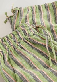 Ensemble short et haut en tissu doux avec des rayures verticales vertes, roses et noires, taille élastique et cordons sur une surface claire.