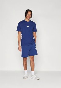 Blaues Sport-Set mit kurzärmligem Shirt und Shorts, mit weißem Adidas-Logo und drei Streifen an den Seiten, aus atmungsaktivem Stoff gefertigt.