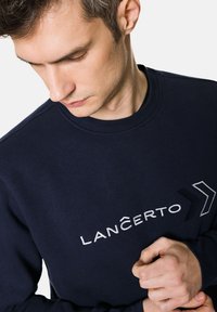Granatowy sweatshirt wykonany z miękkiego materiału, z białym haftem napisu "LANCERTO" oraz wzorem strzały z przodu, z okrągłym dekoltem.