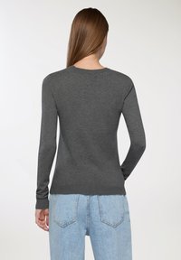 Szary sweter wykonany z dzianiny, z okrągłym dekoltem, długimi rękawami i prążkowanym wykończeniem. Zestawiony z jasnoniebieskimi jeansami o wysokim stanie.