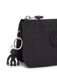 Zwarte stoffen pouch met een gestructureerde afwerking, ritssluiting en een zwart aapvormig bedeltje bevestigd met een zilveren sleutelhanger.