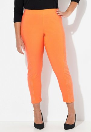 Pantalons de yoga orange avec une coupe ajustée, présentant un accent texturé brillant sur les côtés. Les chevilles resserrées complètent l'ensemble.