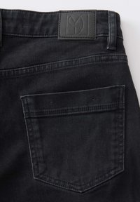 Jeans en denim noir avec une surface texturée, une poche arrière avec des coutures courbes et un patch en cuir rectangulaire embouti sur la taille.