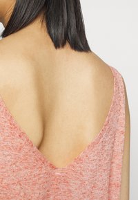 Haut sans manches à col en V, en tissu rouge clair texturé avec un léger motif chiné. Dos et épaules dénudés ; coupe décontractée.