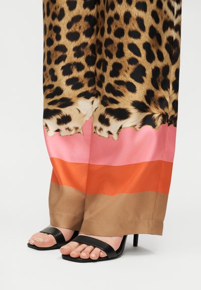 Παντελόνι με φαρδιά καμπάνα σε σχέδιο λεοπάρ με ροζ, πορτοκαλί και μπεζ χρωματιστές μπλοκ, συνδυασμένα με μαύρα πέδιλα με ανοιχτά δάχτυλα και ψηλό τακούνι.