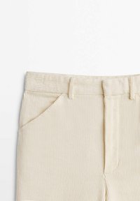 Gros plan sur un pantalon en velours côtelé beige montrant la ceinture, les passants de ceinture, la poche avant et les lignes verticales texturées du tissu.