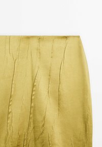 Tissu satin jaune avec des plis verticaux visibles, drapé à plat sur un fond blanc.