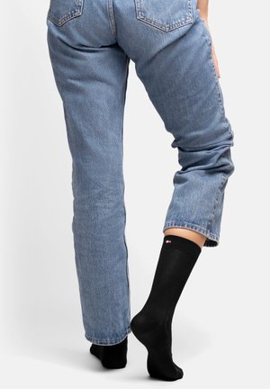 Sorte knælange sokker med et lille logo ved kanten, parret med lyseblå højtaljede denimjeans med en afslappet pasform og opfoldede ben.