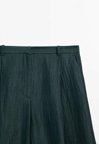 Pantalon en tissu vert foncé texturé, montré à partir de la taille avec passants de ceinture, poches et une fermeture frontale cachée.