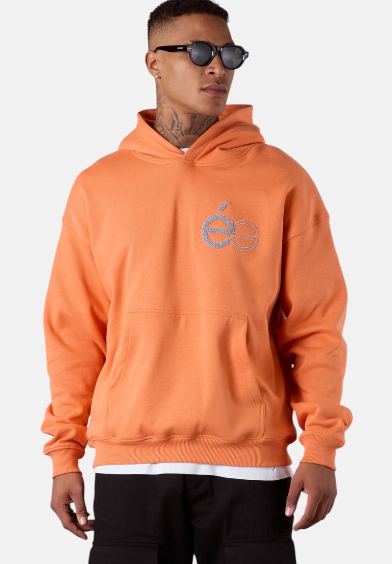 Sweat à capuche orange avec une poche dans le devant, un cordon de serrage pour la capuche et un logo brodé. Le tissu semble doux, avec des poignets et un ourlet côtelés.