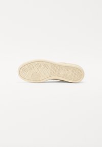 Beige sneaker zool met een circulair patroon en een getextureerd profiel voor grip. Gladde oppervlakte met verhoogde accenten en een ronde neusvorm.