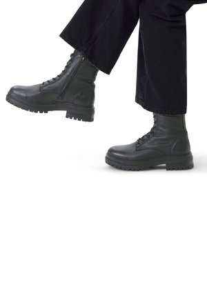 Zwarte leren legervoetbalschoenen met een gestructureerde afwerking, vetersluiting en stevige rubberen zolen. De broek is zwart en cropped net boven de enkel.