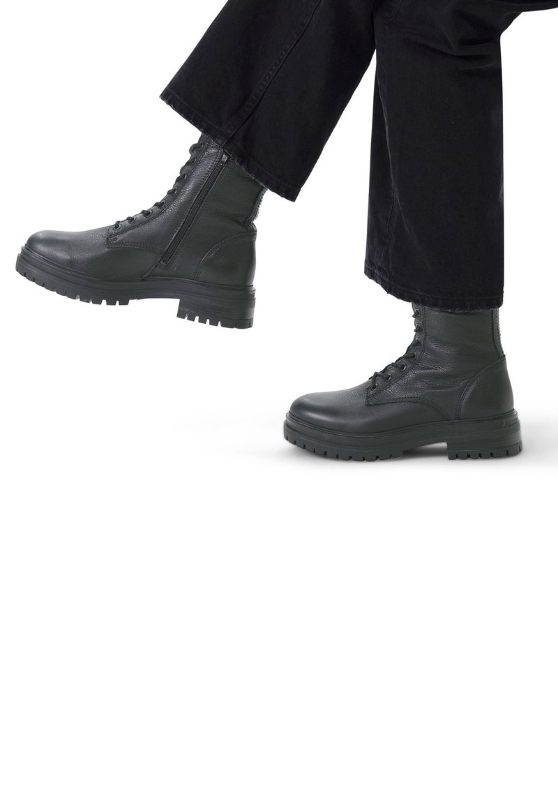 Zwarte leren legervoetbalschoenen met een gestructureerde afwerking, vetersluiting en stevige rubberen zolen. De broek is zwart en cropped net boven de enkel.