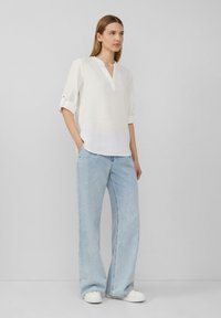 Haut en lin blanc avec un décolleté en V et des manches roulées, associé à un jean large bleu clair et des baskets blanches. Style simple et décontracté.