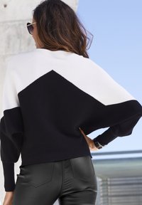 Knit sweater featuring a black, white, and black color block design, with a loose fit and ribbed texture. Paired with black fitted pants.